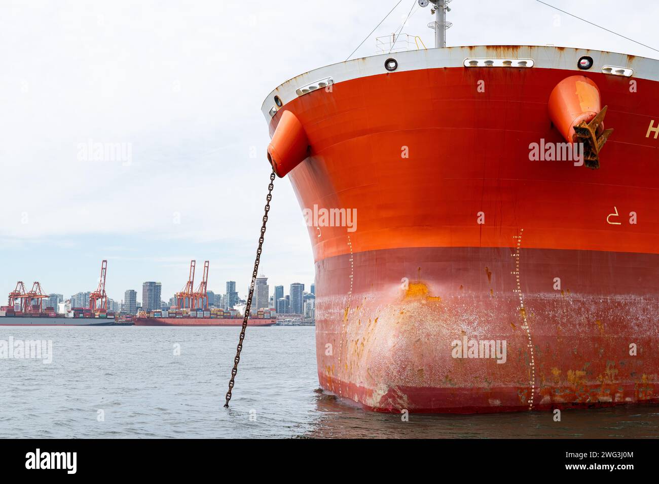 La proa de un buque de contenedores que está anclado en el puerto de Vancouver con el horizonte de Vancouver, Columbia Británica en el fondo. Foto de stock