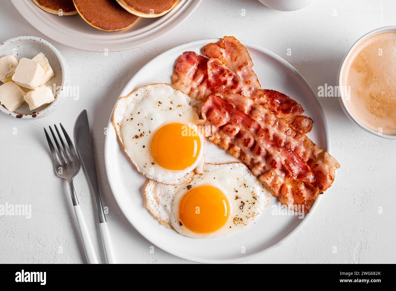 Desayuno con huevos fritos, tocino, tortitas y café, vista superior. Huevos fritos soleados con tocino en el plato y café cappuccino de la mañana. Bre americano Foto de stock