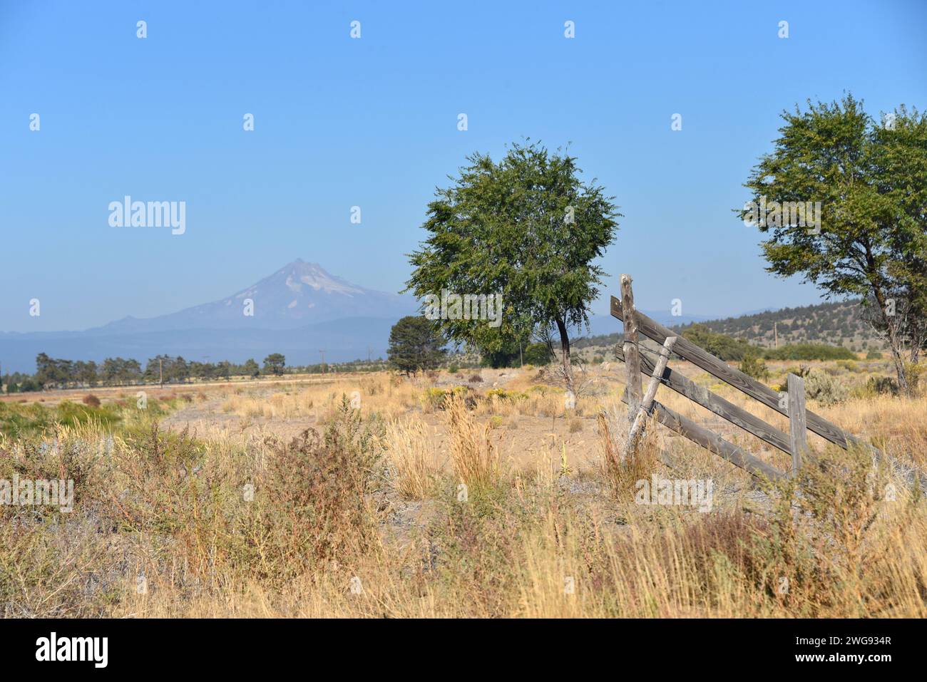 El poste rústico de la cerca sentado en un campo, en Oregon, enmarca las hermosas montañas Cascade. Foto de stock
