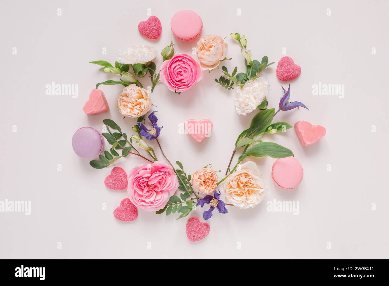 Vista aérea de un arreglo floral de rosas, crisantemos, flores de alstroemeria y follaje alrededor de caramelos en forma de corazón sobre un fondo rosa Foto de stock