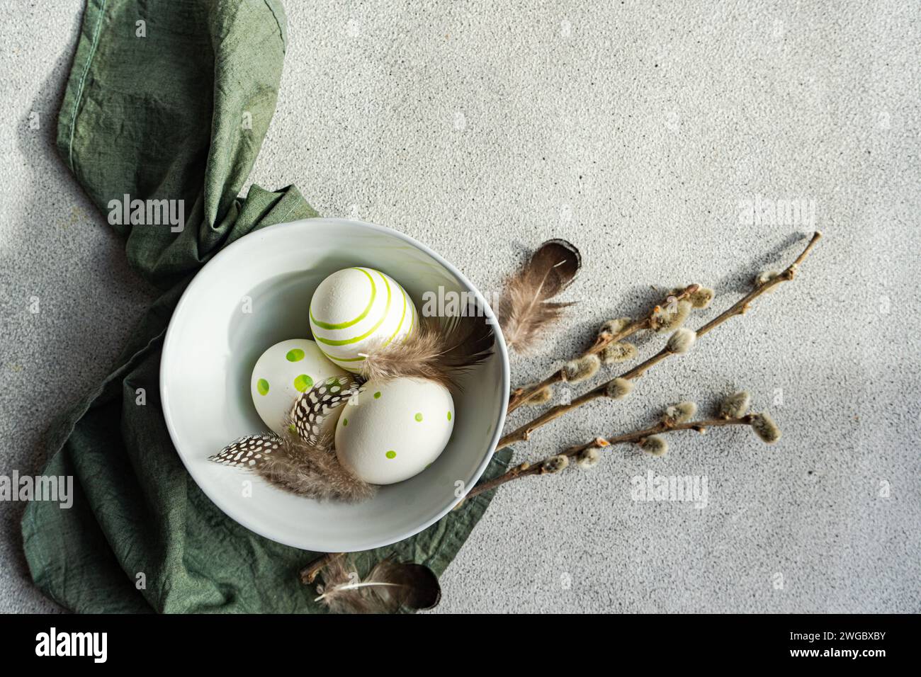Primer plano del arreglo festivo de Pascua con huevos de Pascua pintados, ramas de sauce coño y plumas en un tazón junto a una servilleta Foto de stock