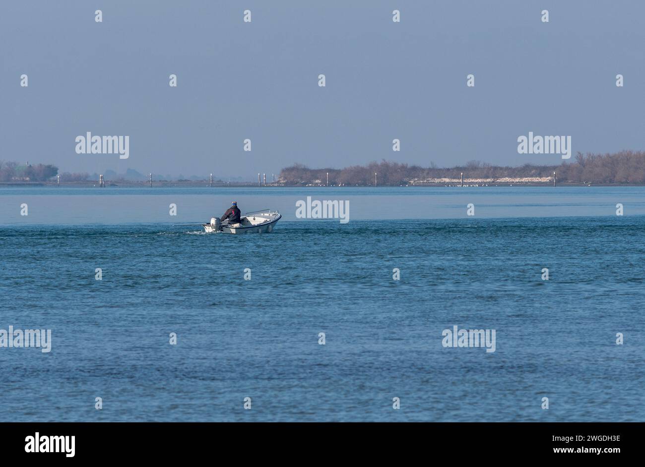 Un pequeño barco pesquero con pescador de edad avanzada a bordo regresa al puerto después de un viaje de inspección en un día de invierno nebuloso en Grado, Italia. Foto de stock