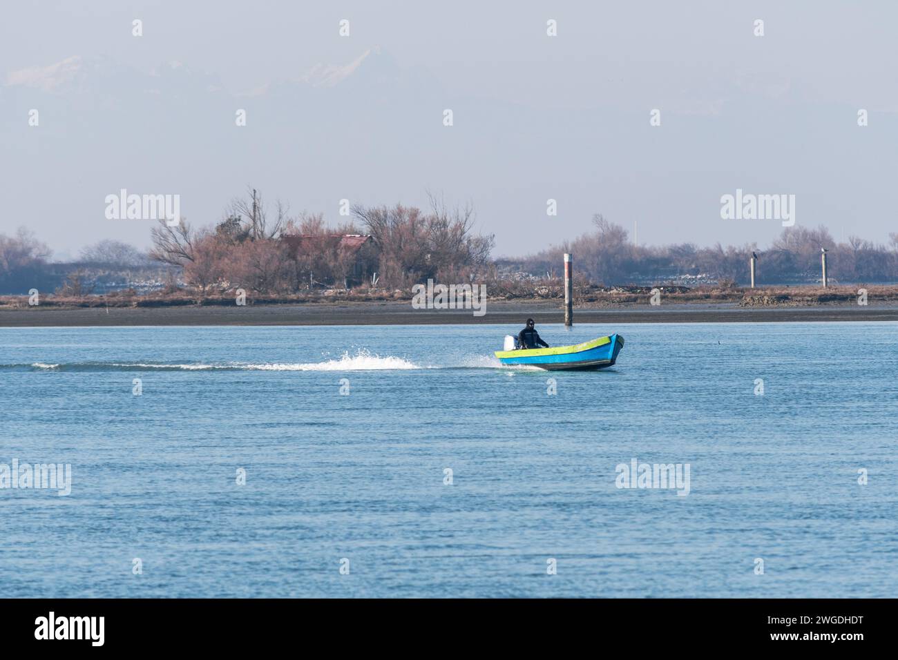 Un pequeño barco pesquero con pescador a bordo regresa a puerto a gran velocidad después de un viaje de inspección en un día de invierno nebuloso en Grado, Italia. Foto de stock