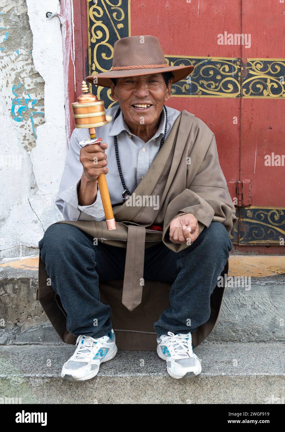 Un hombre gira una rueda de oración tibetana mientras está sentado en escalones de piedra en la Plaza Barkhor, Lhasa. Foto de stock