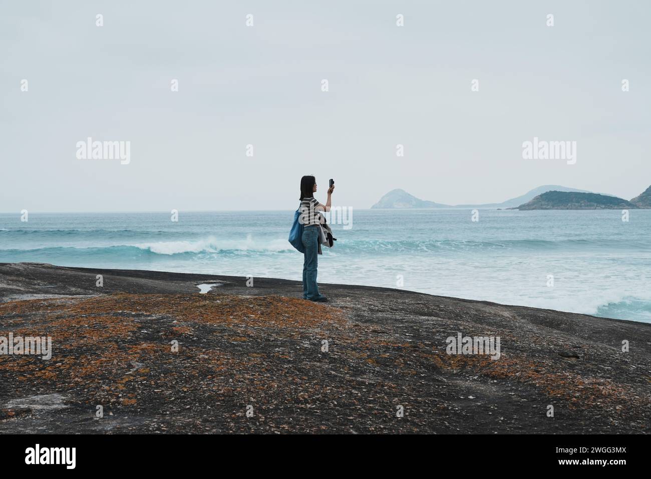 Una mujer asiática con una camisa de rayas, tomando una foto del mar Foto de stock
