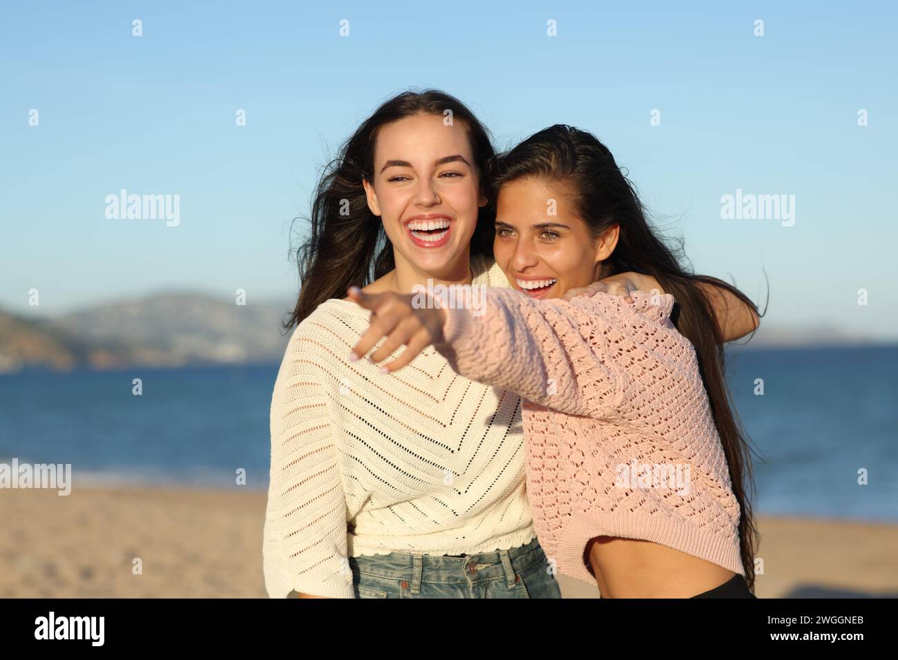 Dos amigos divertidos señalando en la playa al atardecer Foto de stock