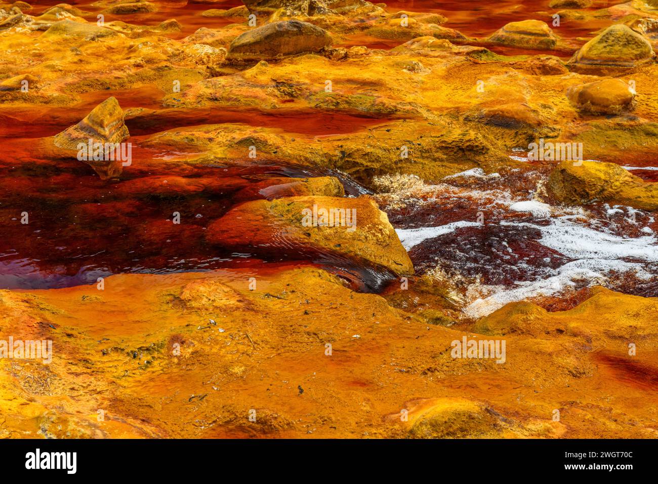 El agua espumosa se precipita sobre las rocas coloridas y cargadas de hierro en el río Rio Tinto Foto de stock