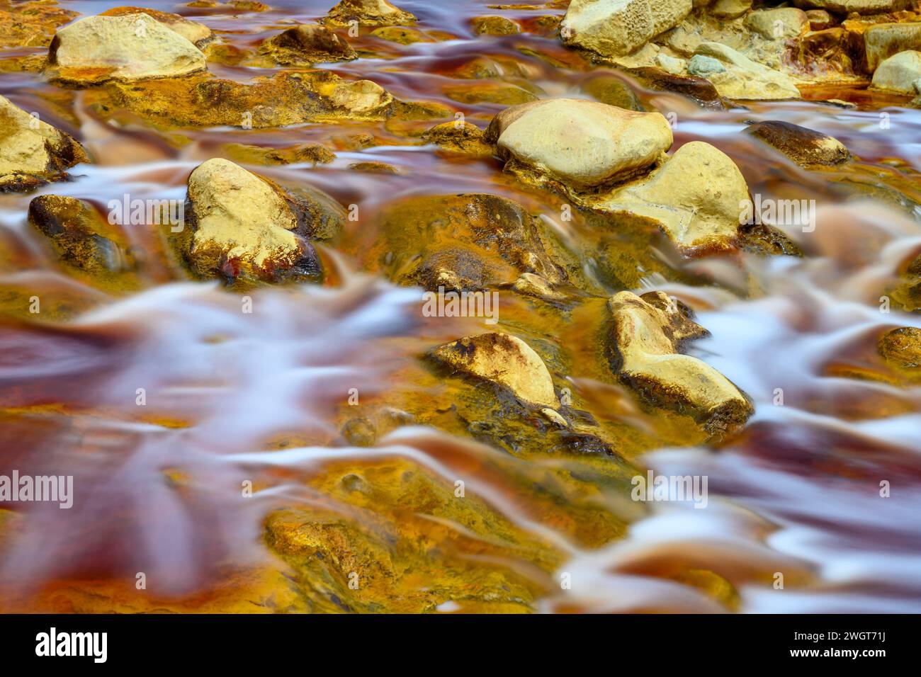 El agua espumosa se precipita sobre las rocas coloridas y cargadas de hierro en el río Rio Tinto Foto de stock