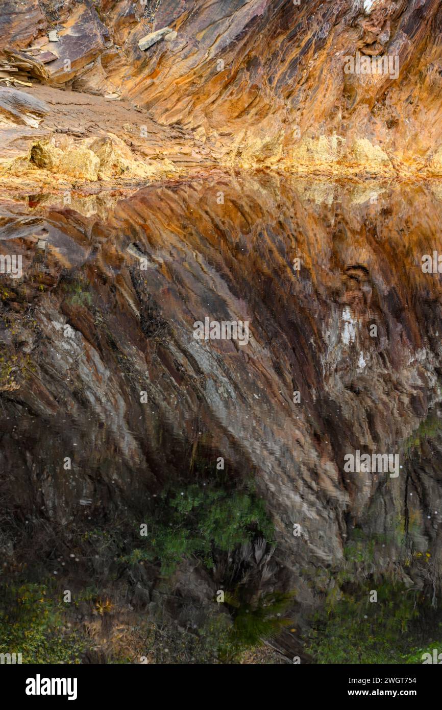 Los acantilados ricamente estriados del Río Tinto se reflejan perfectamente en las tranquilas aguas del río, creando una simetría natural Foto de stock