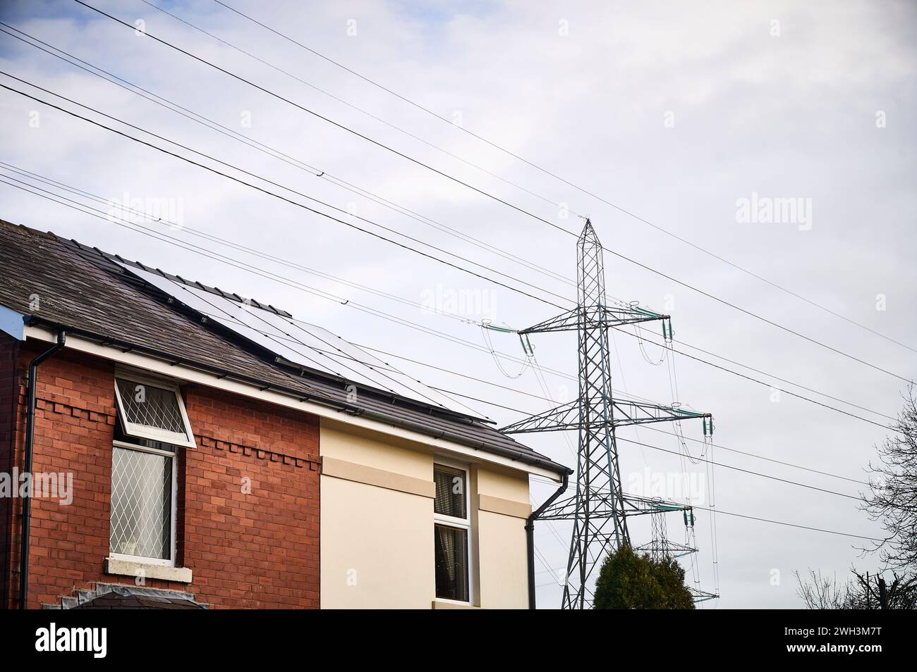 Casa con paneles solares en el techo que se sienta debajo de las líneas eléctricas de la red nacional y el pilón que muestra dos formas de generación de electricidad Foto de stock