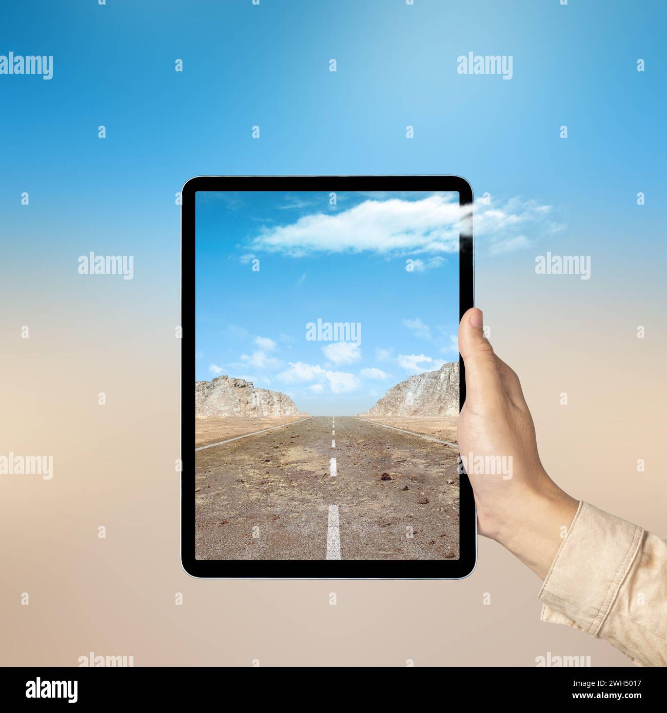 Mano humana que sostiene la tableta con una vista de la pantalla de una calle con colinas y vista del acantilado de roca con el cielo azul. Concepto de viaje Foto de stock