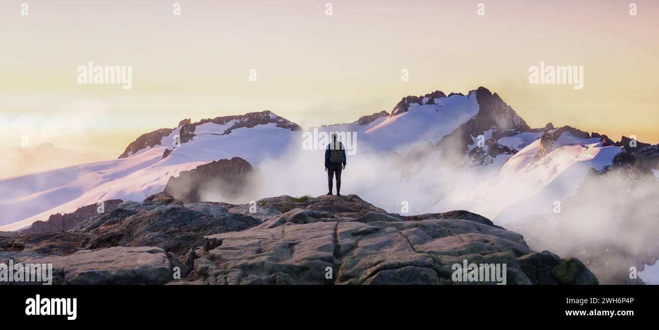 Aventurero Hombre Hiker en la cima del pico. Montañas en el fondo. Aventura Compuesto 3d Renderizado. Imagen aérea del paisaje de BC, Canadá. Puesta de sol Foto de stock