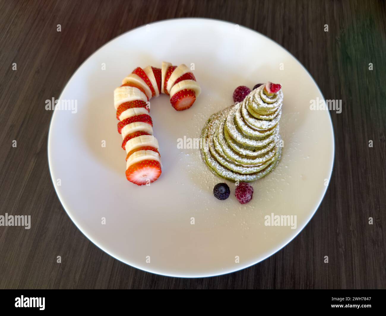 Un desayuno navideño con un árbol de Navidad de panqueques y una caña de dulces de plátano y fresa. Foto de stock