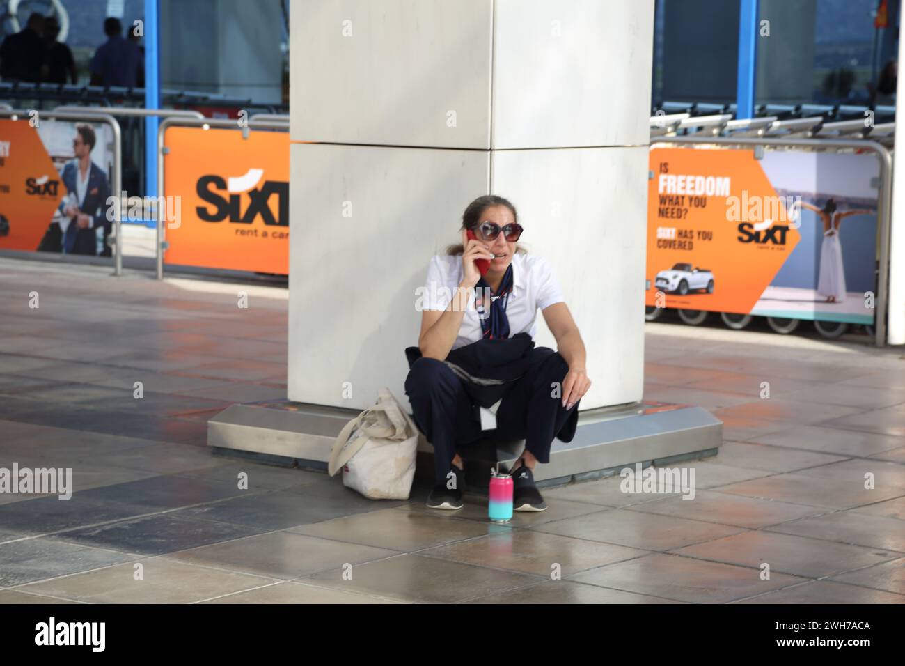 Atenas Grecia Aeropuerto Internacional de Atenas (AIA) Eleftherios Venizelos Mujer agazapada fuera de la Terminal Dos al hablar por teléfono móvil Foto de stock