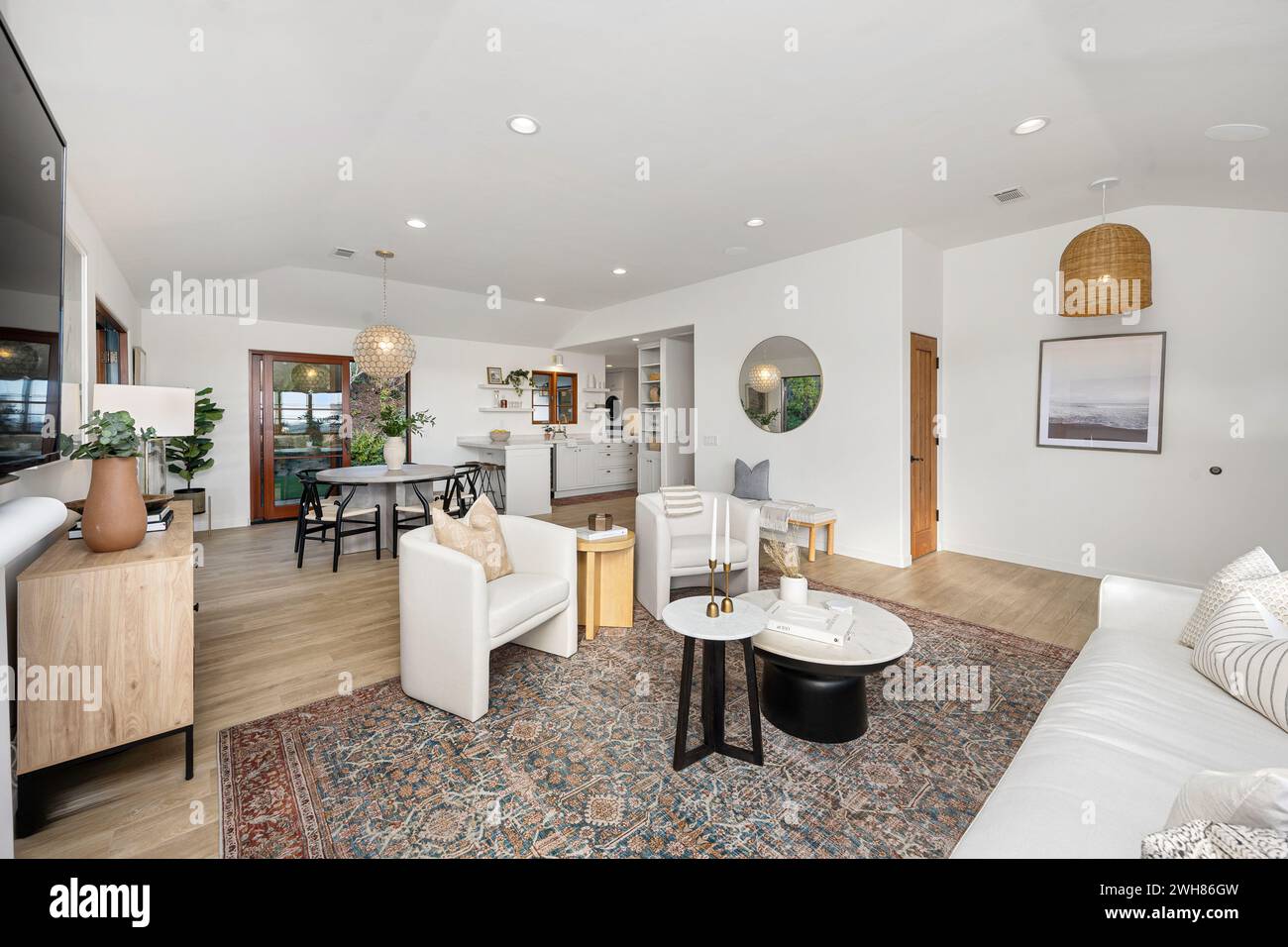 Muebles blancos y amplias ventanas adornan una sala de estar bellamente diseñada, con un televisor Foto de stock