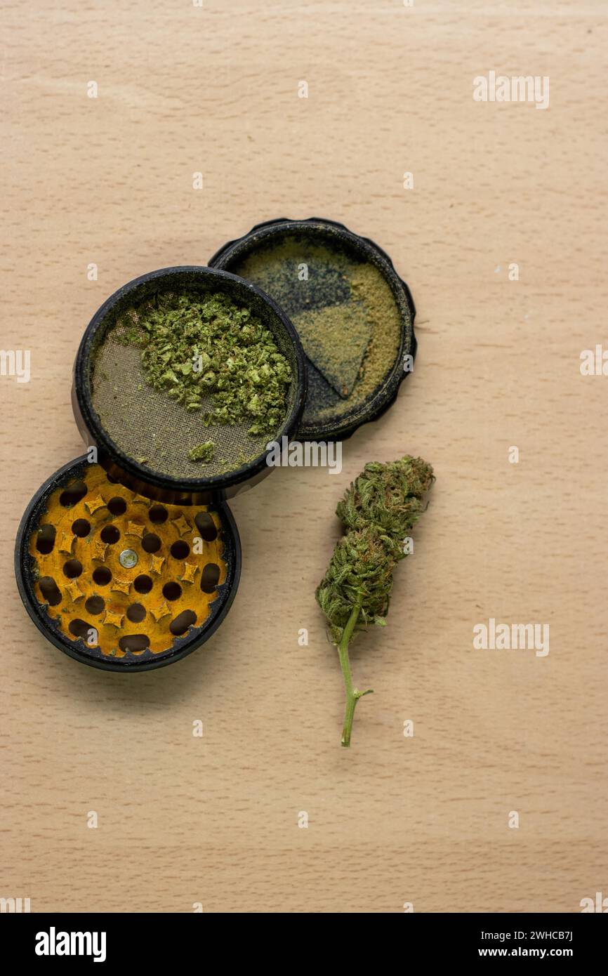 Imagen vertical de un molinillo para prensar marihuana con un cogollo junto a él sobre una superficie de madera Foto de stock