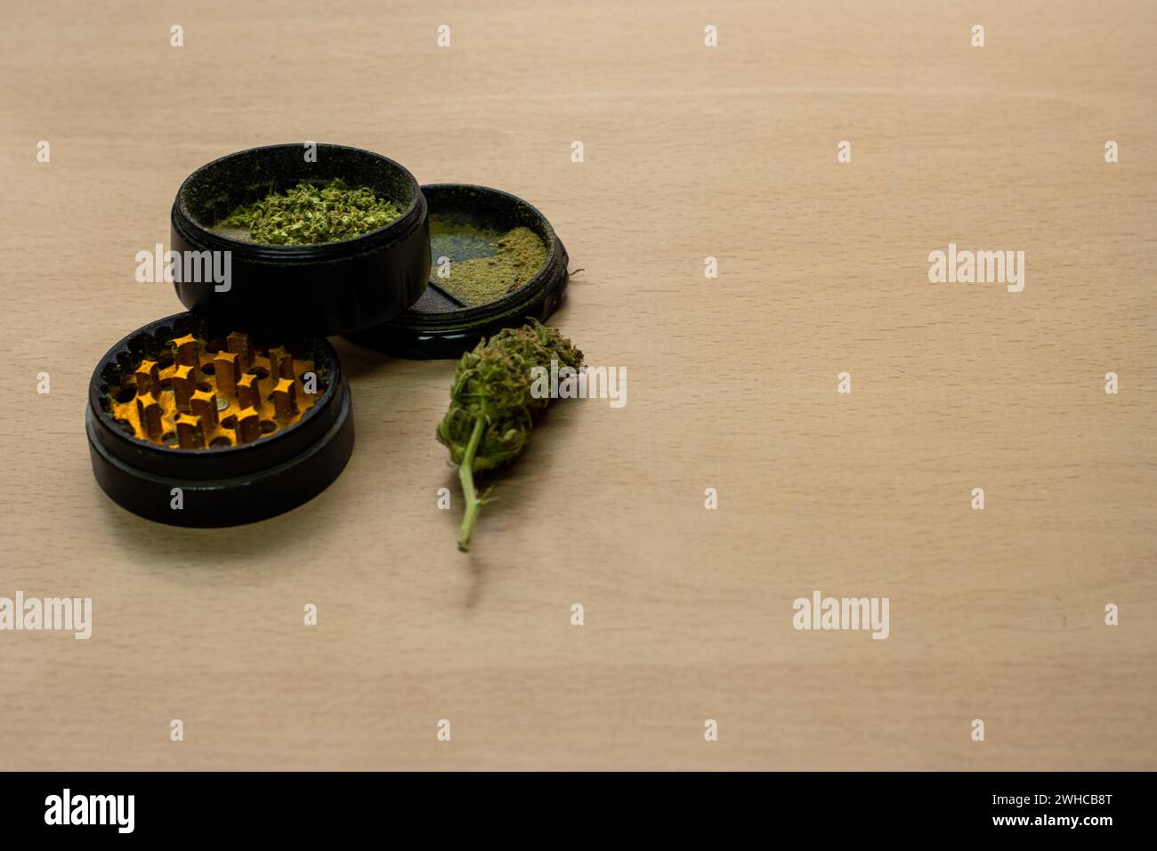 Un molinillo para presionar marihuana con un brote junto a ella sobre una superficie de madera Foto de stock