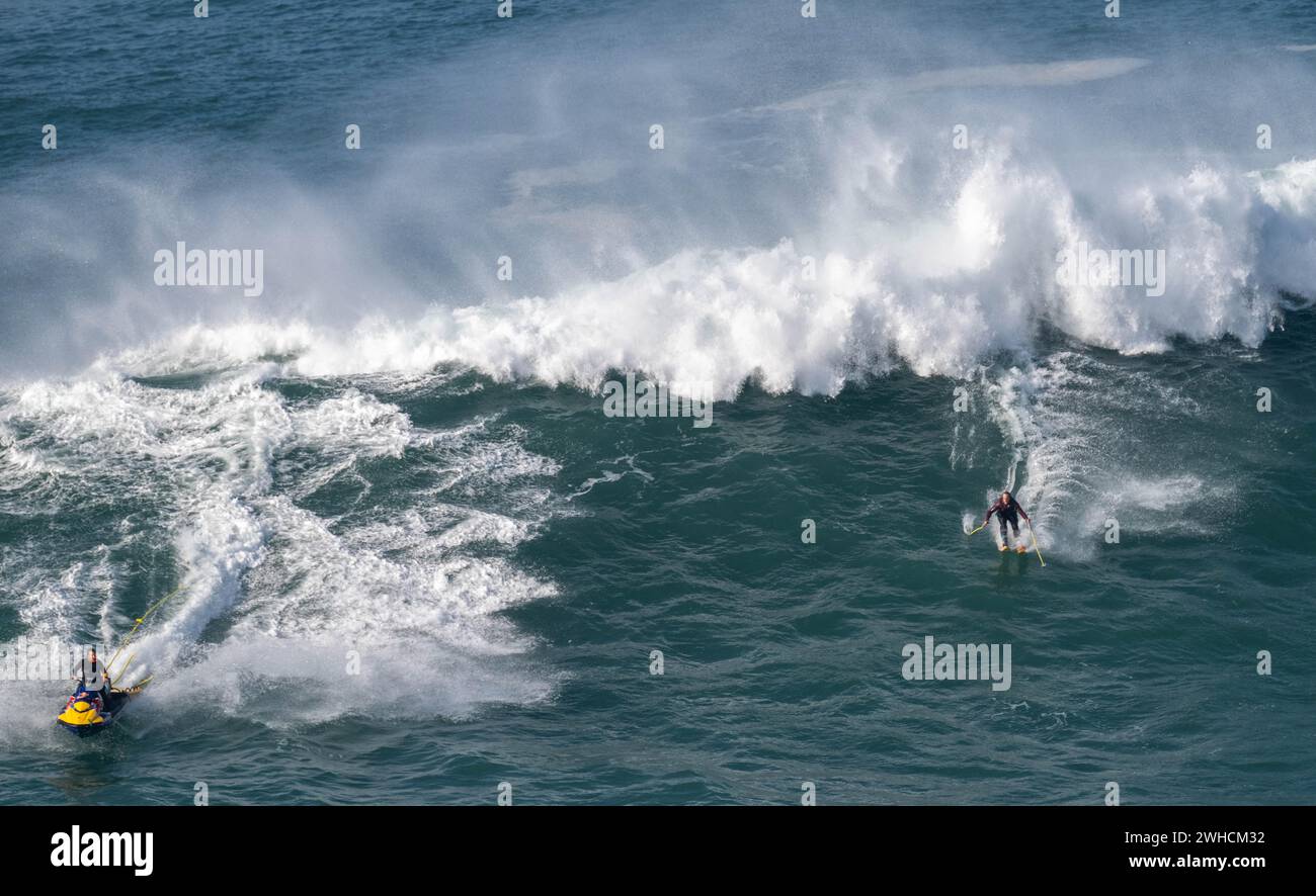 Un esquiador acuático con bastones montando una gran ola y una moto acuática junto a él, Nazare, Portugal Foto de stock