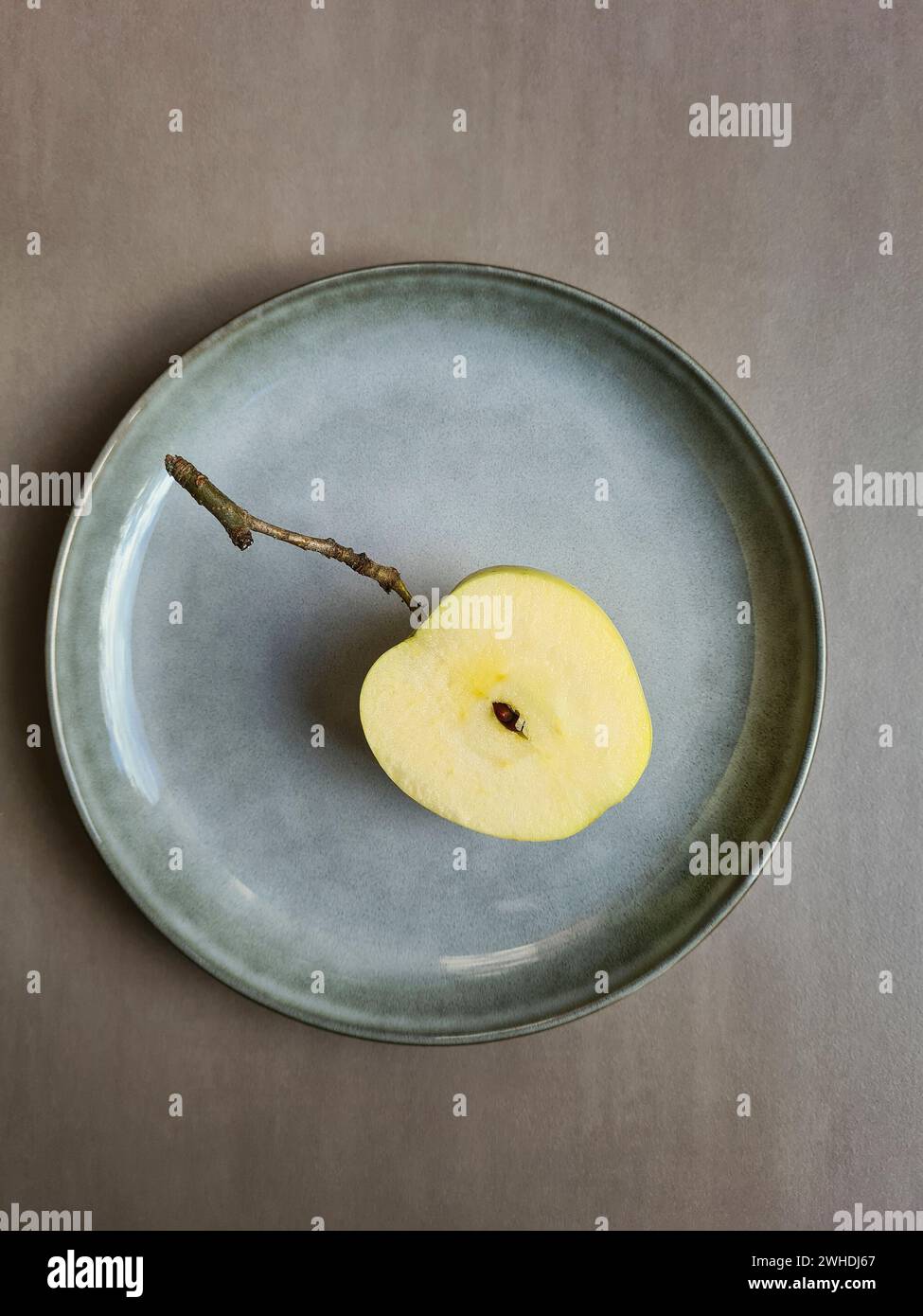 Una manzana fresca a la mitad con núcleo se encuentra en un plato de color pastel y fondo gris claro Foto de stock