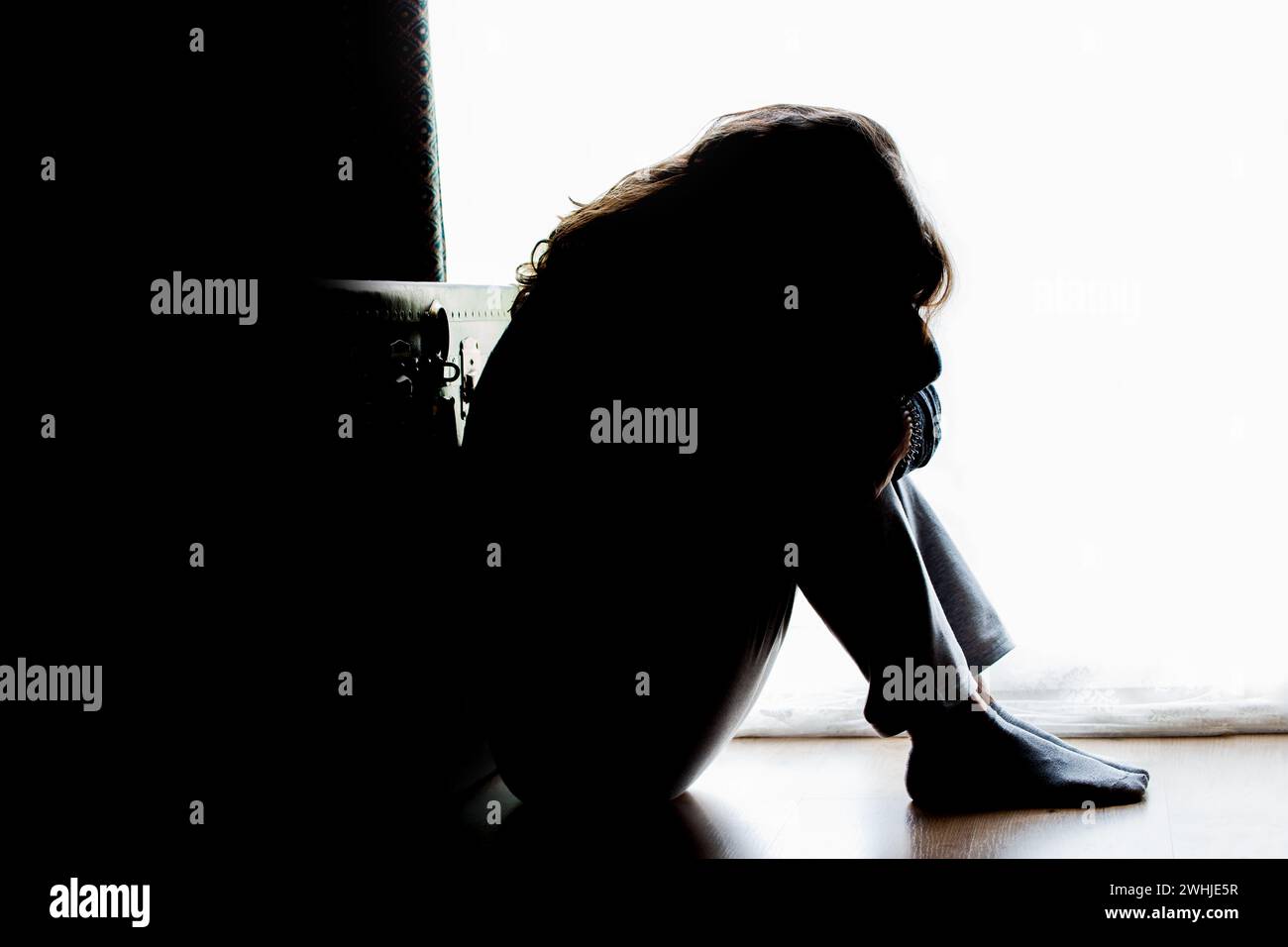 Infeliz mujer madura, mujer en silueta, sentado en el suelo con la espalda iluminada. Pensamientos deprimentes. Foto de stock