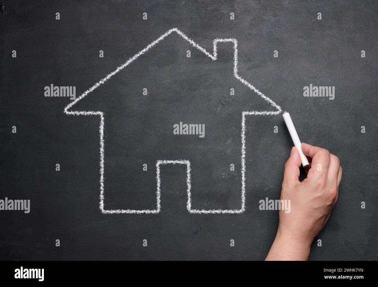 Una mano femenina dibujada con tiza en una pizarra una casa en miniatura, concepto de alquiler, hipoteca Foto de stock