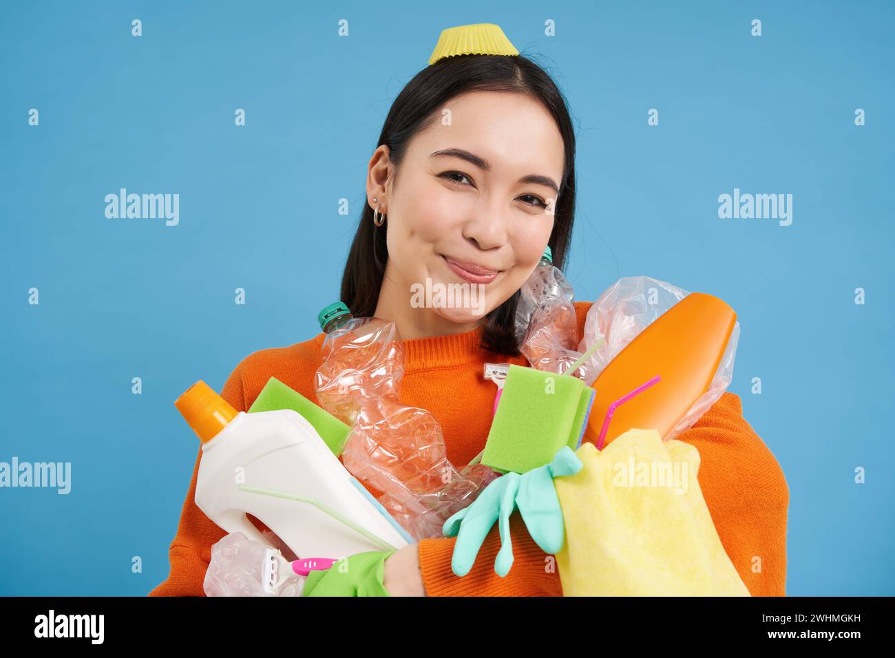 Retrato de mujer coreana entusiasta, sosteniendo botellas de plástico vacías, clasificando la basura, sonriendo y mirando feliz, aislado en bl Foto de stock