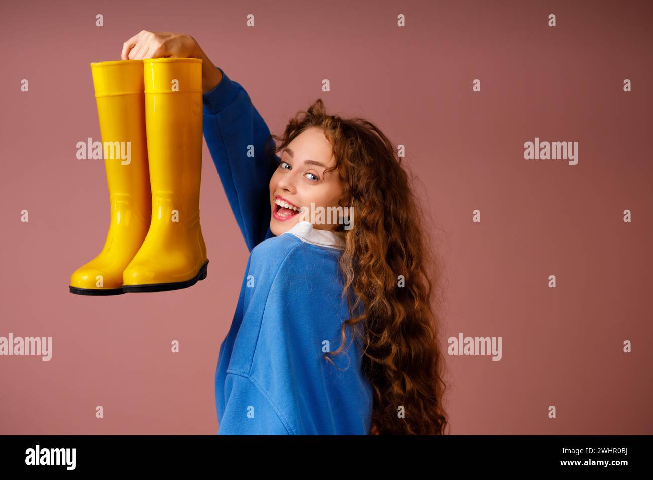 Mujer sonriente positiva joven sostiene en sus manos unas botas de goma. Foto de stock