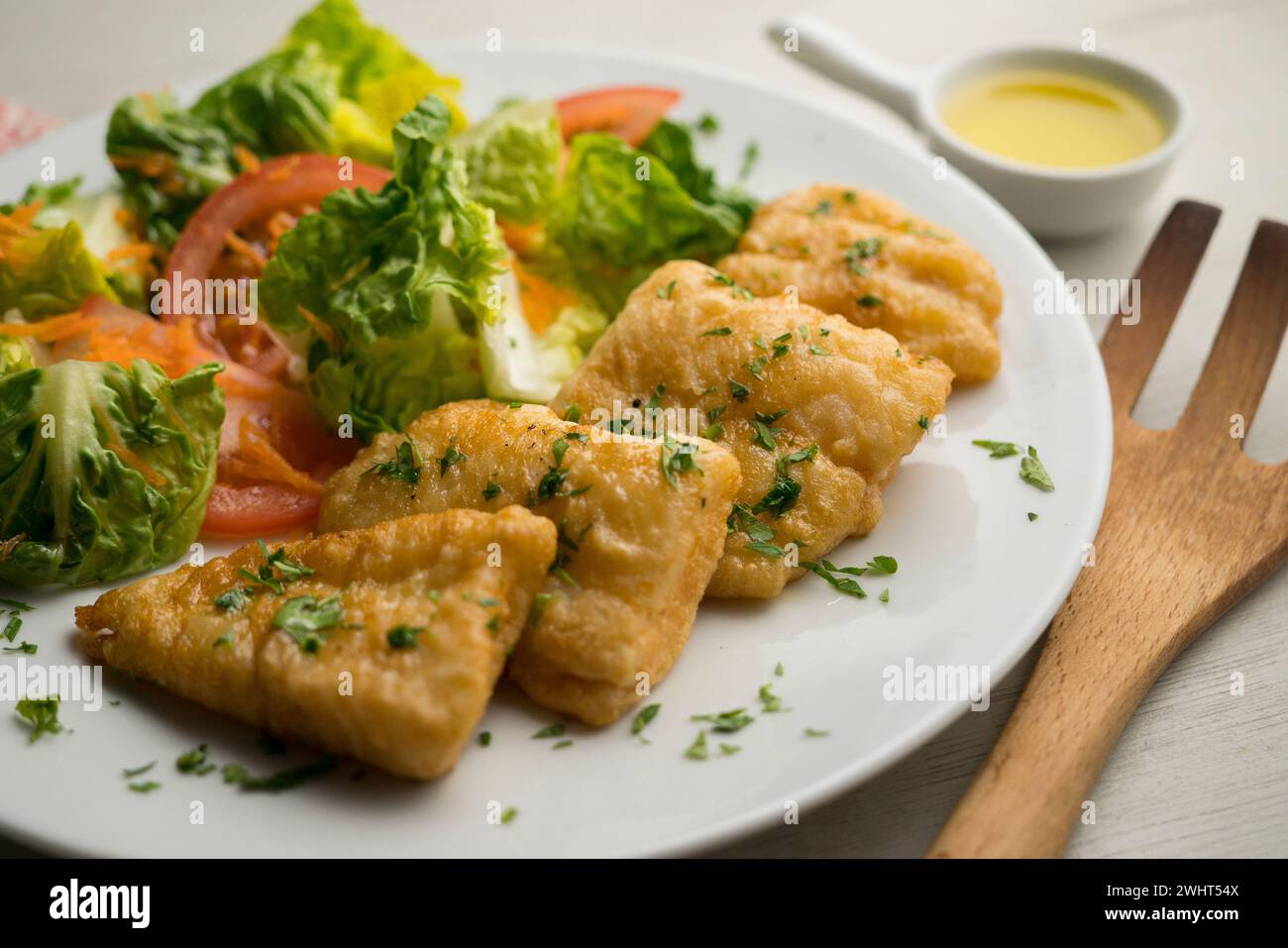 Pescado blanco batido servido con una ensalada de tomate. Foto de stock