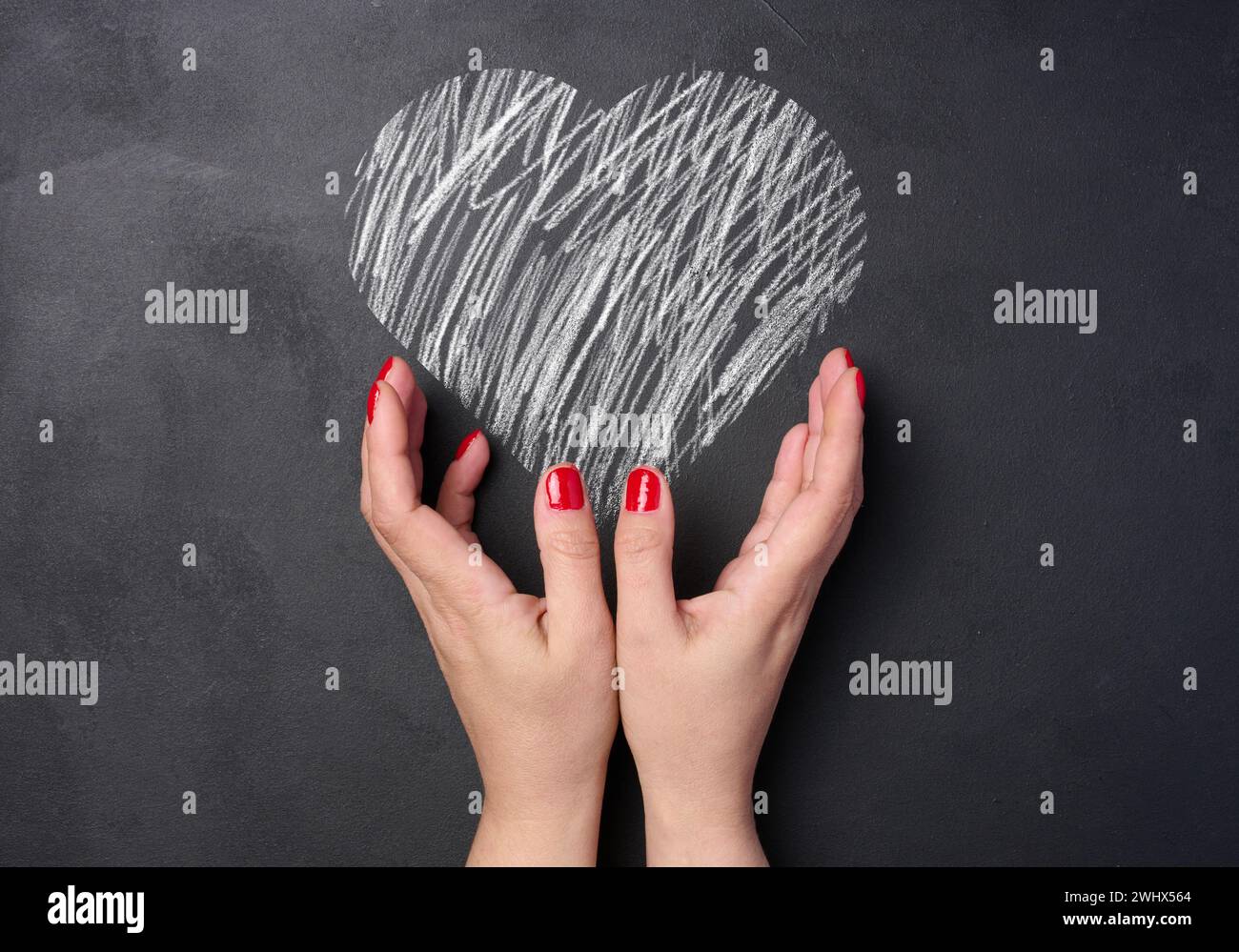 Un corazón dibujado con tiza blanca sobre un tablero negro y dos manos femeninas Foto de stock