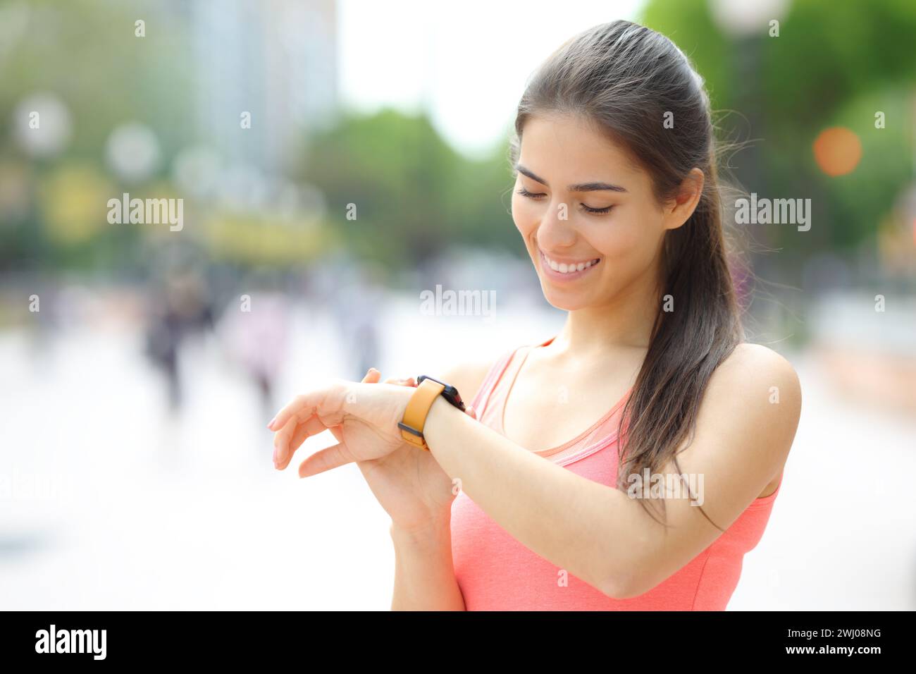 Corredor feliz comprobando el tiempo en smartwatch después de correr en la calle Foto de stock