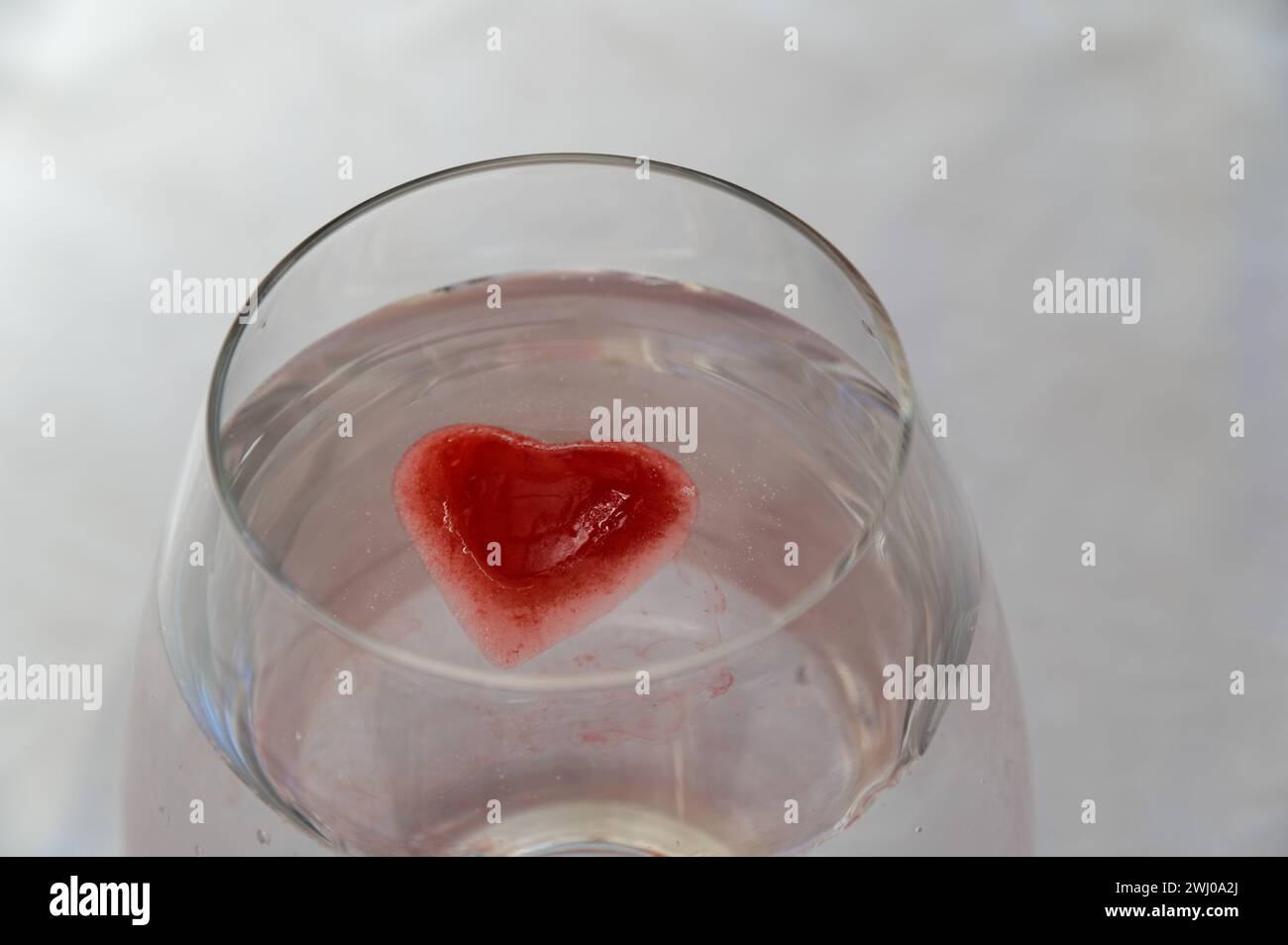 Un cubo de hielo rosa se está derritiendo en el líquido claro en el vidrio Foto de stock