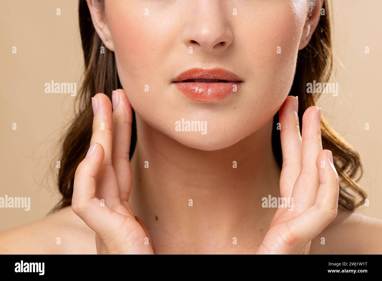 Mujer caucásica con el pelo castaño que lleva maquillaje natural sobre fondo beige Foto de stock
