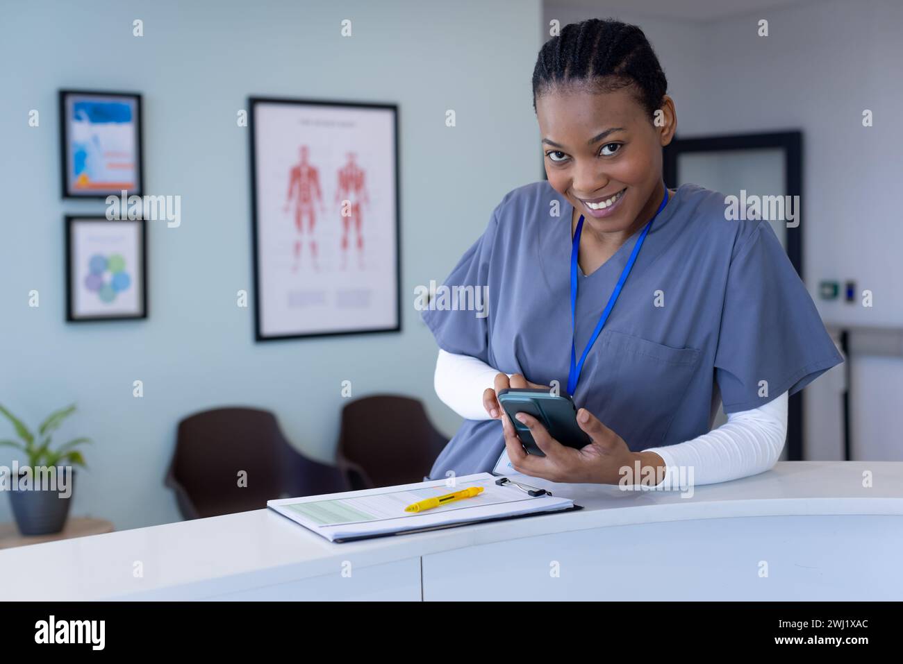 Retrato del médico femenino afroamericano feliz usando smartphone en la recepción del hospital Foto de stock