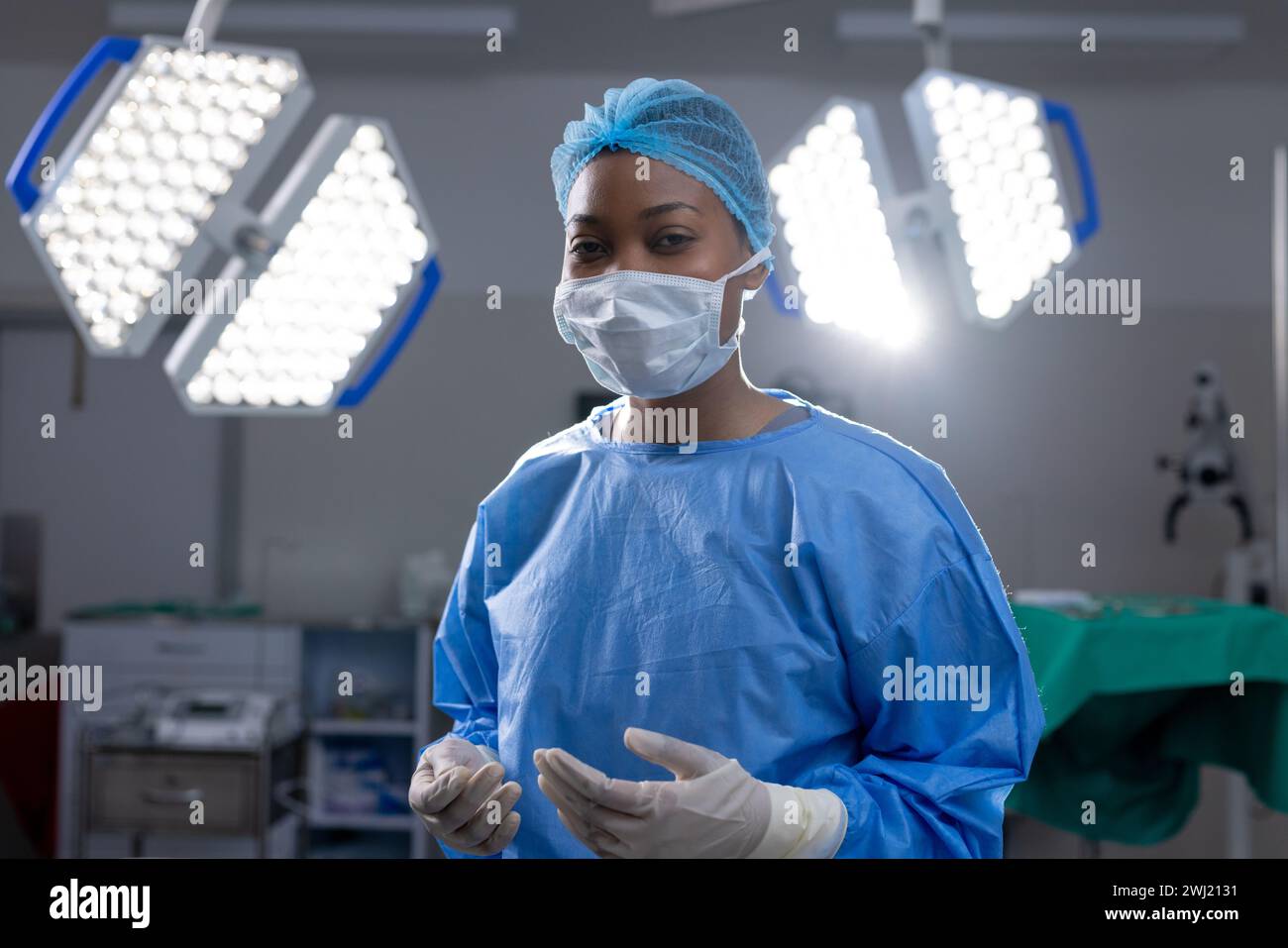 Retrato del médico femenino afroamericano con máscara facial y guantes en sala de operaciones del hospital Foto de stock