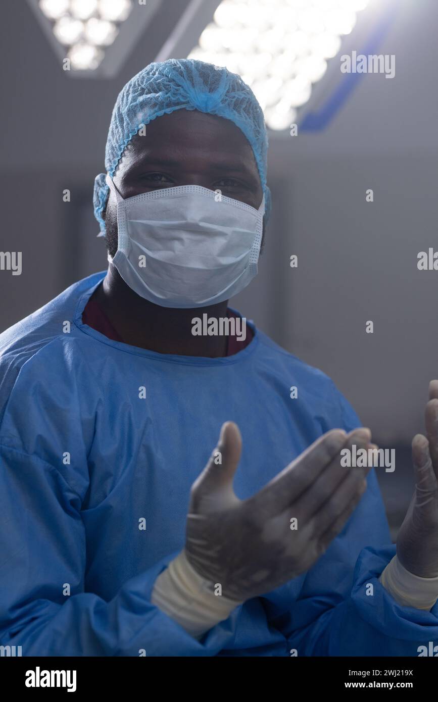 Retrato del médico masculino afroamericano con máscara facial y guantes en el quirófano del hospital Foto de stock