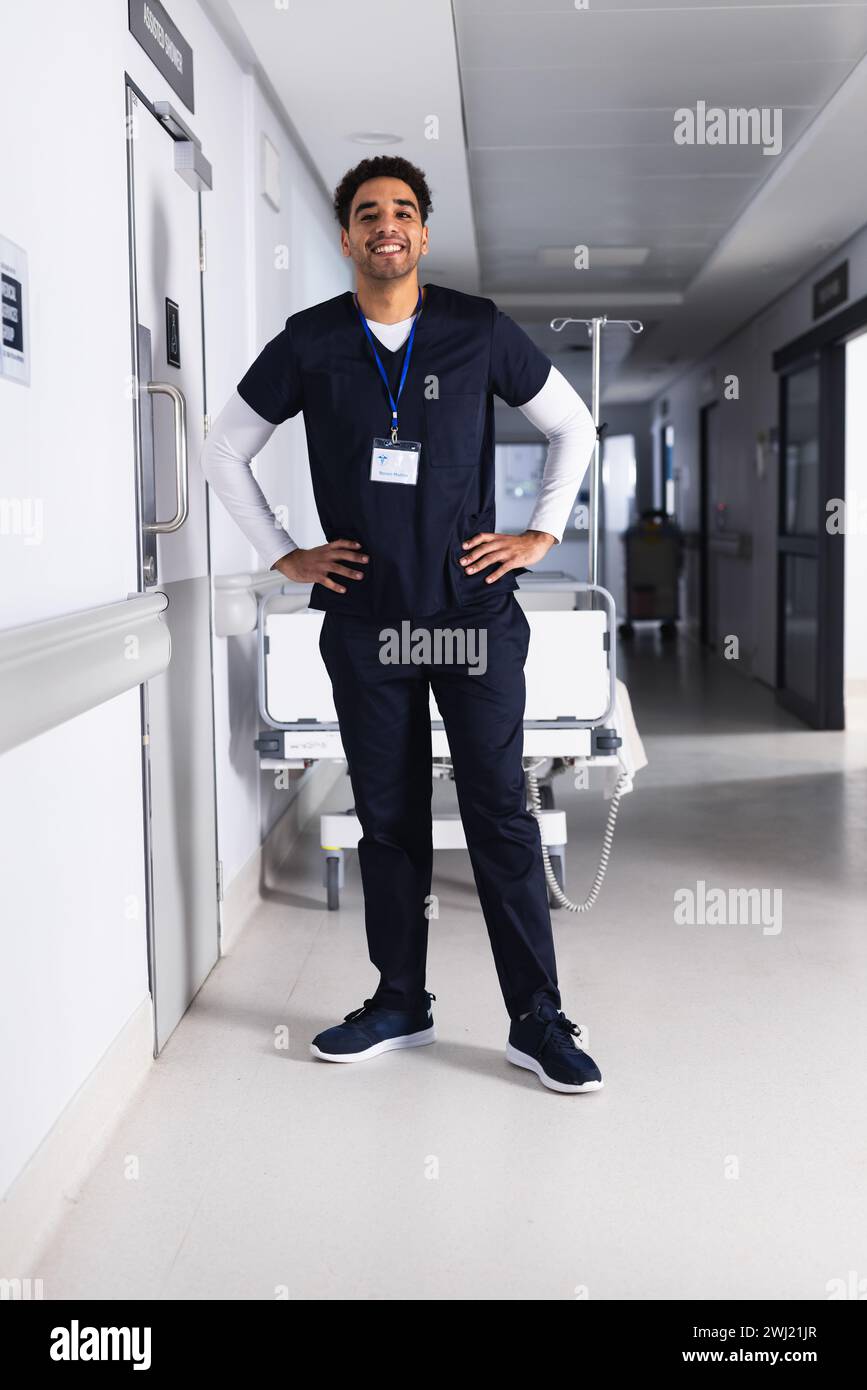 Retrato del médico masculino biracial feliz de pie en el pasillo del hospital Foto de stock