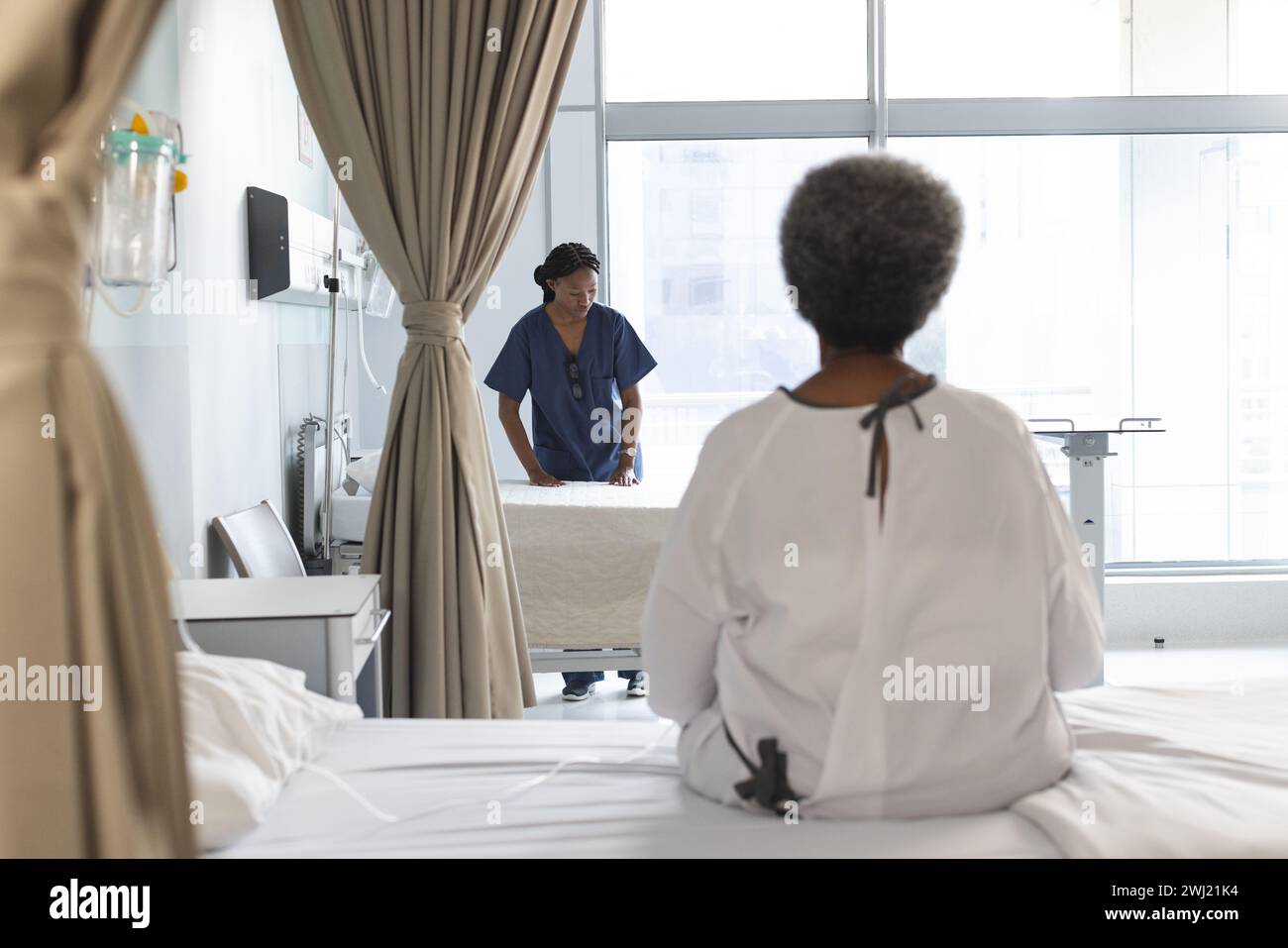 Parte posterior del paciente femenino mayor afroamericano sentado en la cama en la soleada habitación del hospital Foto de stock