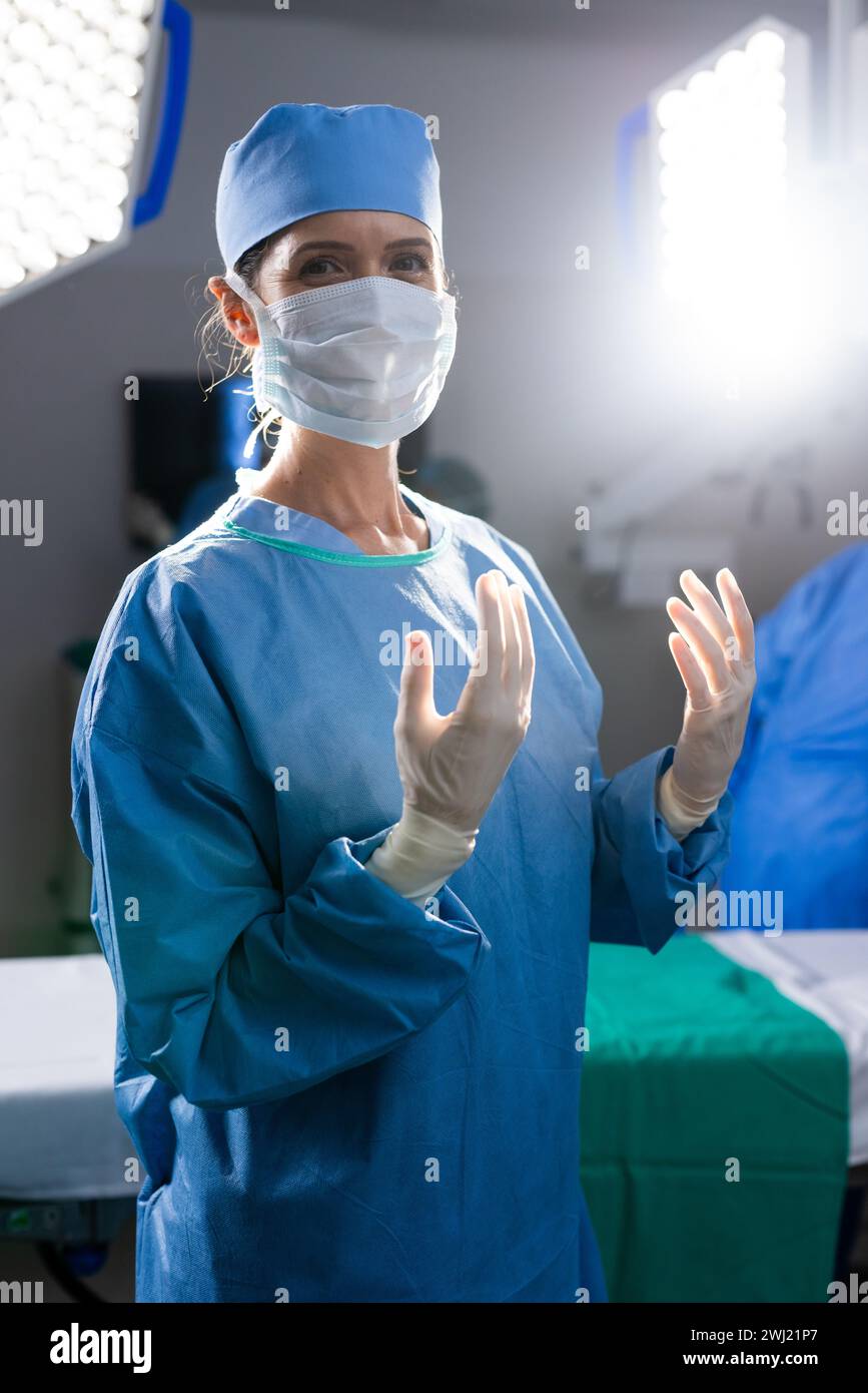 Retrato de la doctora caucásica con máscara facial y guantes protectores en el quirófano del hospital Foto de stock
