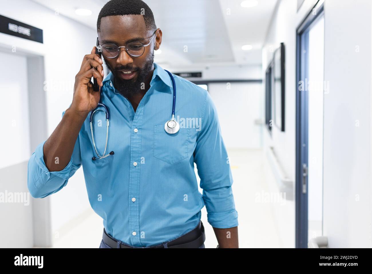Médico masculino afroamericano hablando en teléfono inteligente en pasillo en el hospital, espacio de copia Foto de stock