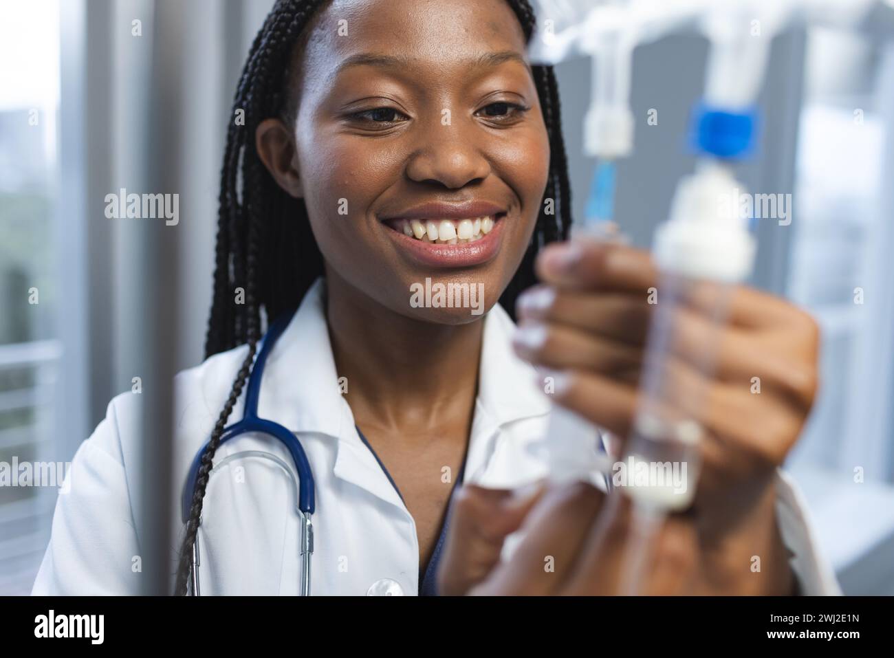 Médico femenino afroamericano feliz que lleva la capa de laboratorio que aplica goteo en la habitación del hospital Foto de stock
