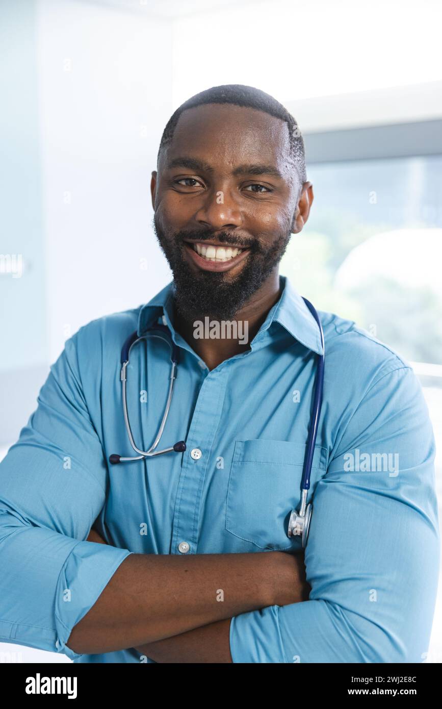 Retrato del médico masculino afroamericano feliz que lleva camisa azul y estetoscopio en la habitación del hospital Foto de stock