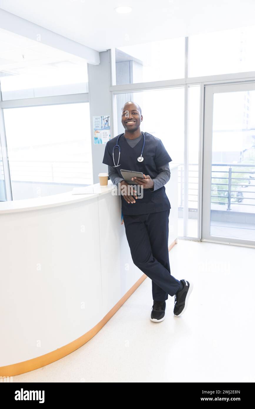 Retrato del médico masculino afroamericano que sostiene la tableta en el mostrador de recepción en el hospital, espacio de la copia Foto de stock