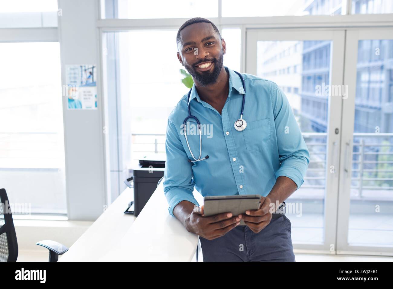 Retrato del médico masculino afroamericano que sostiene la tableta en el mostrador de recepción en el hospital, espacio de la copia Foto de stock