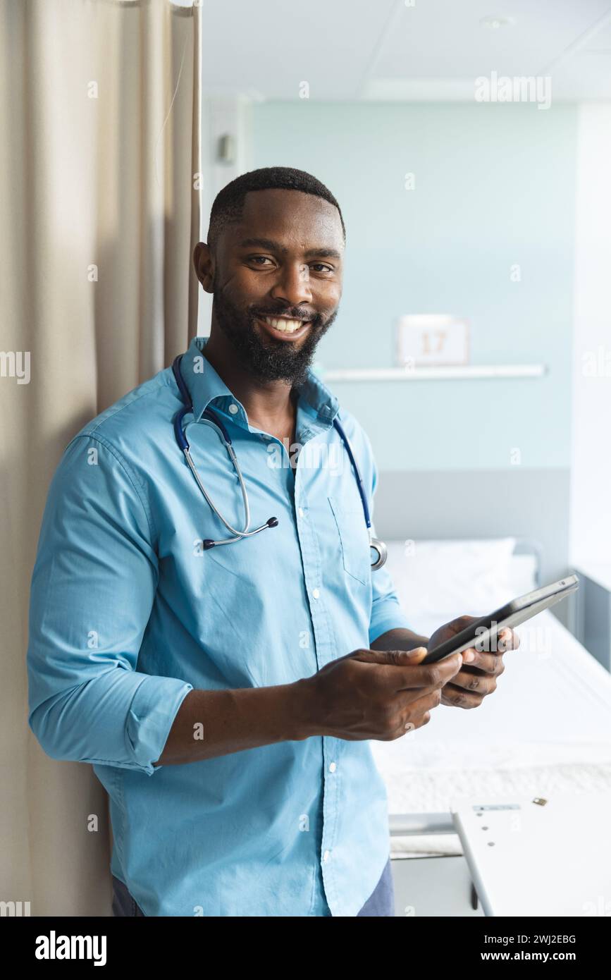 Retrato del médico masculino afroamericano feliz usando la tableta en la habitación del hospital Foto de stock