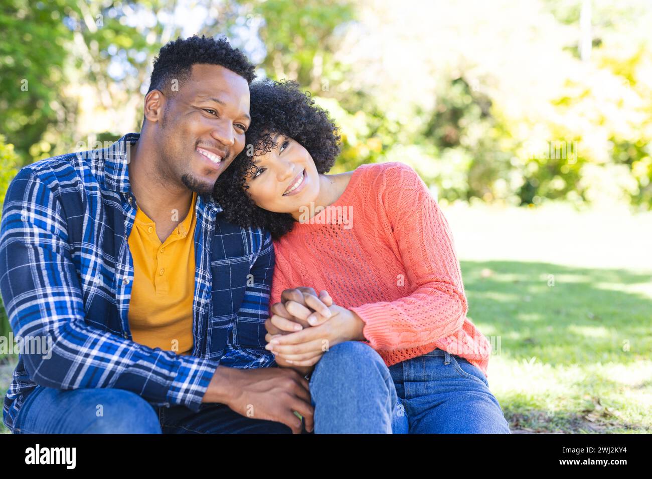 Feliz pareja afroamericana abrazando y sosteniendo de la mano en las escaleras en el jardín soleado, espacio de copia Foto de stock