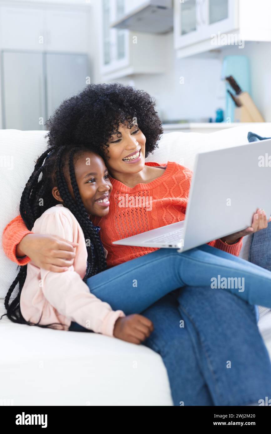 Feliz madre e hija afroamericana abrazando en el sofá y usando el ordenador portátil en casa, espacio de copia Foto de stock