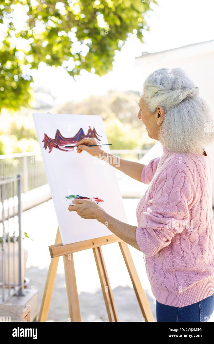 Mujer mayor caucásica pintando sobre lienzo en terraza soleada Foto de stock