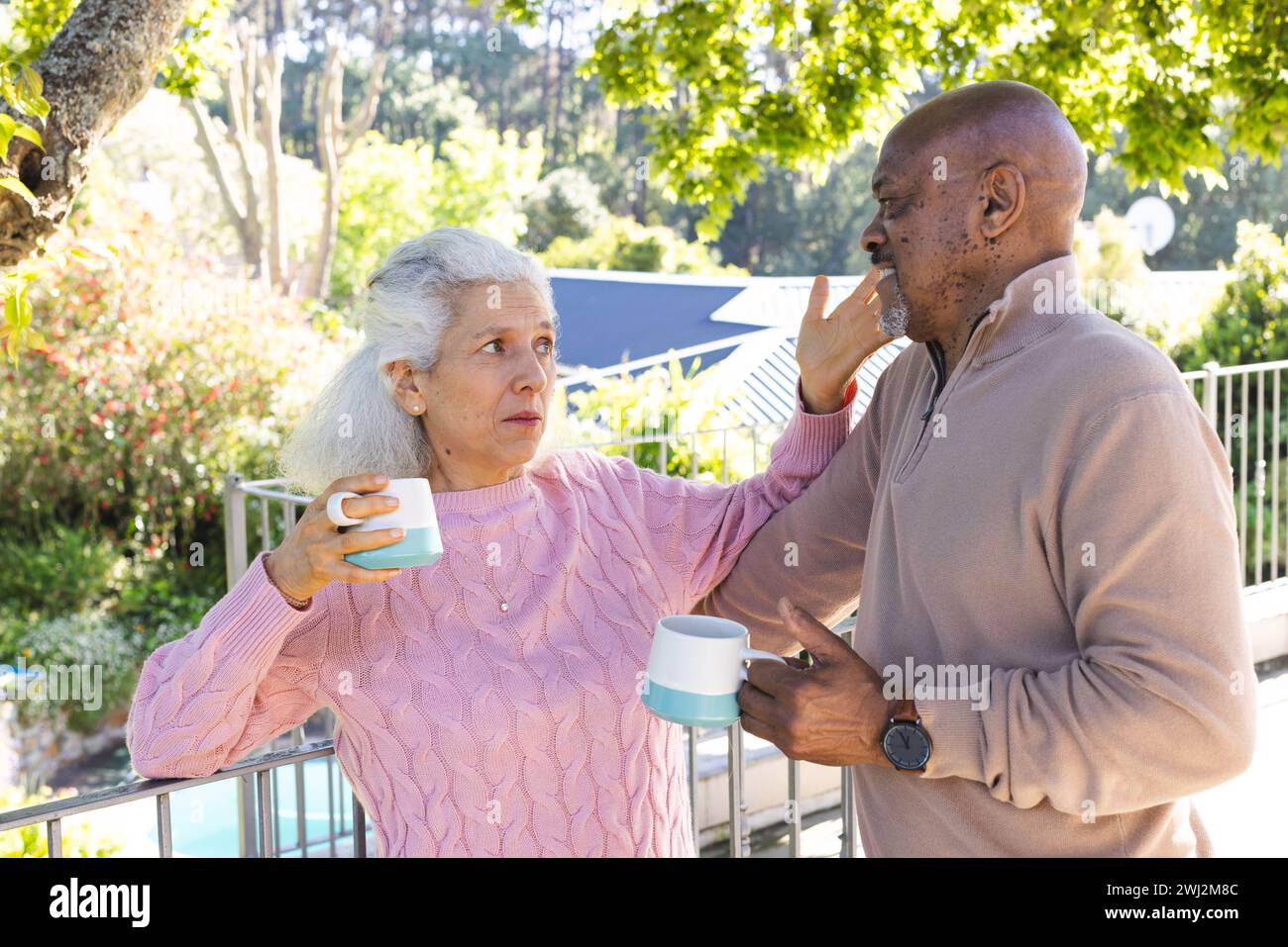 Diversa pareja senior bebiendo café y hablando en la terraza soleada Foto de stock