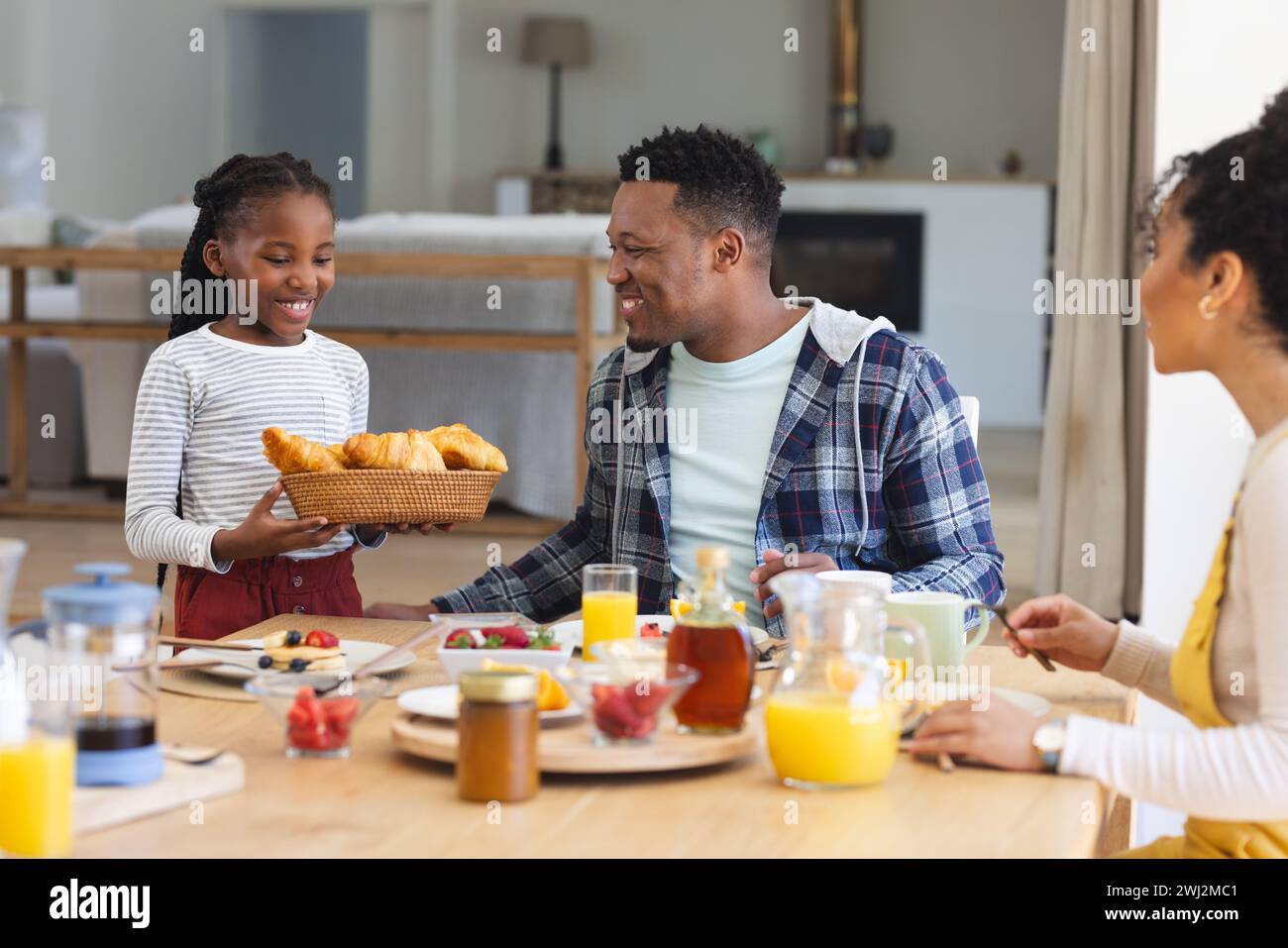 Chica afroamericana feliz que trae la cesta de croissants en la mesa en casa, espacio de copia Foto de stock