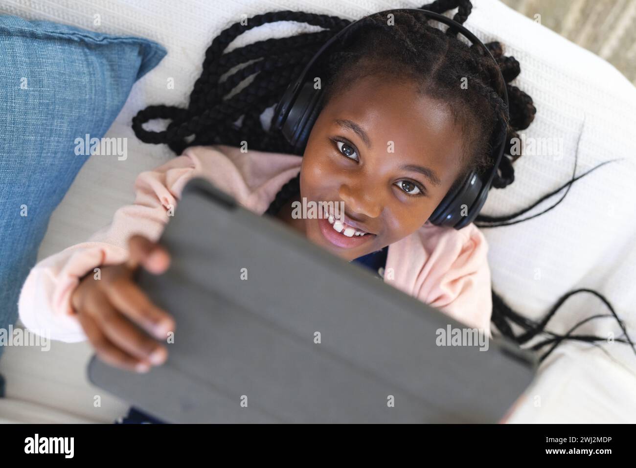 Chica afroamericana feliz acostada en el sofá, escuchando música y usando tableta en casa, copiar espacio Foto de stock